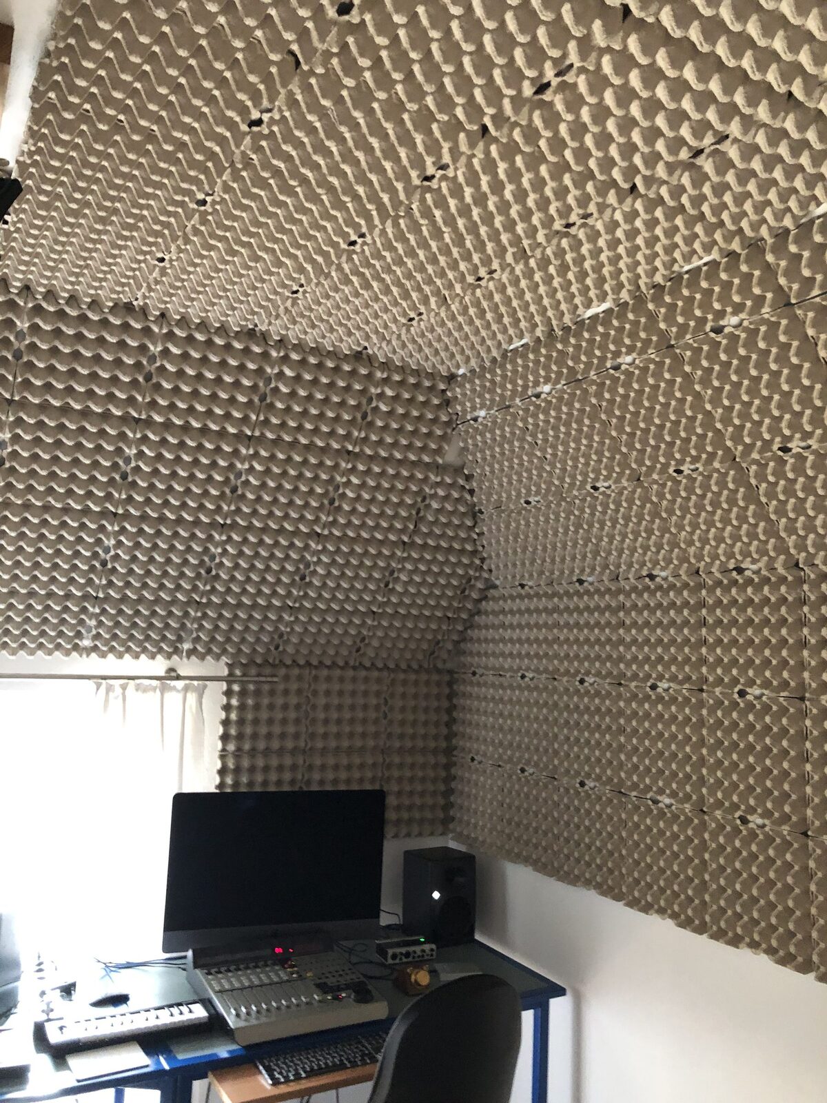 Mein Tonstudio von innen: Decke und Wände sind mit Akustikschaum verkleidet, unten links der Arbeitsplatz mit iMac, Studiomonitor, Mischpult und Keyboard am Fenster.